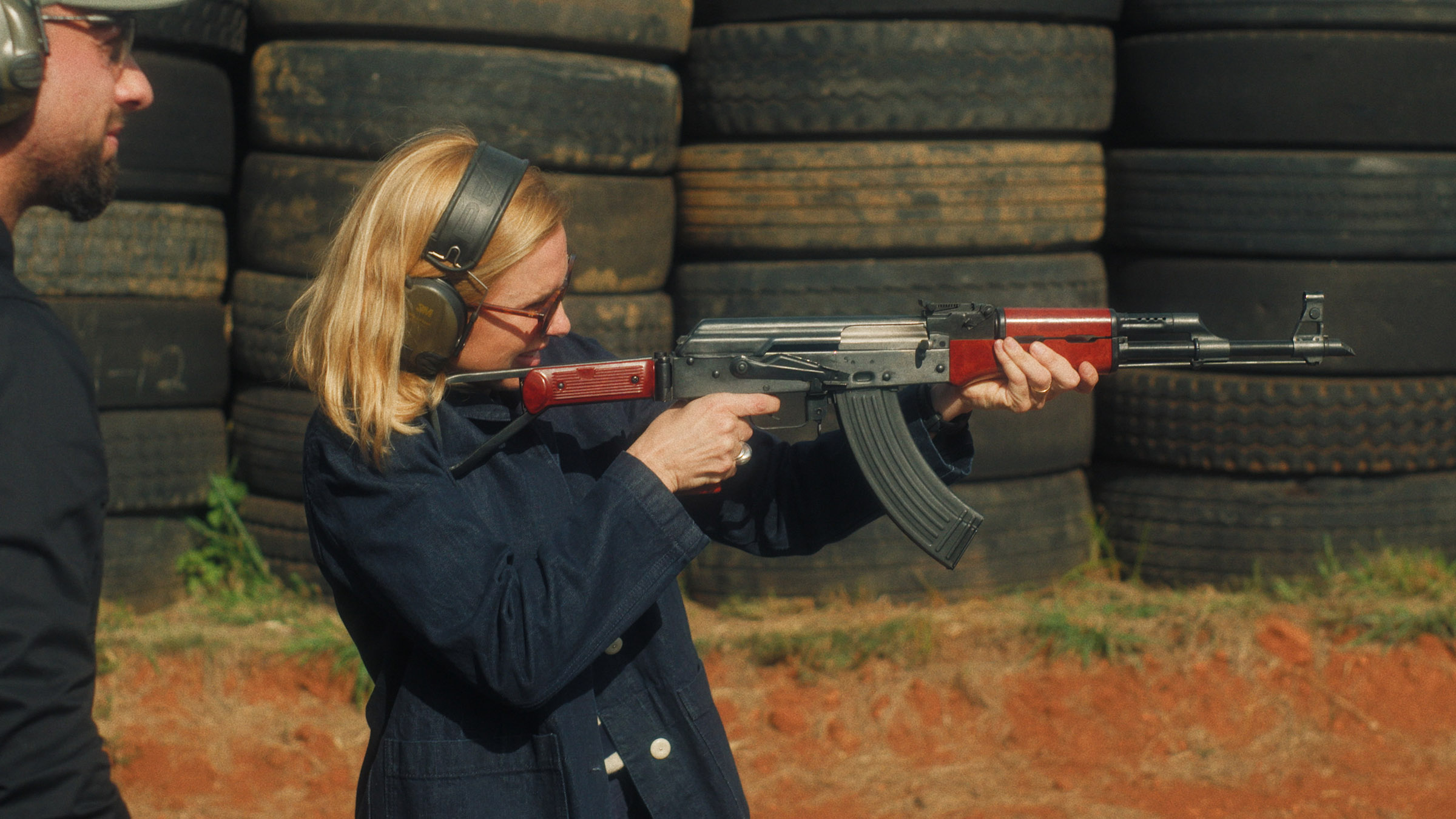 Jose watches as Mariana van Zeller aims a gun at bullet-proof glass in Johannesburg, South Africa. [Photo of the day - August 2025]