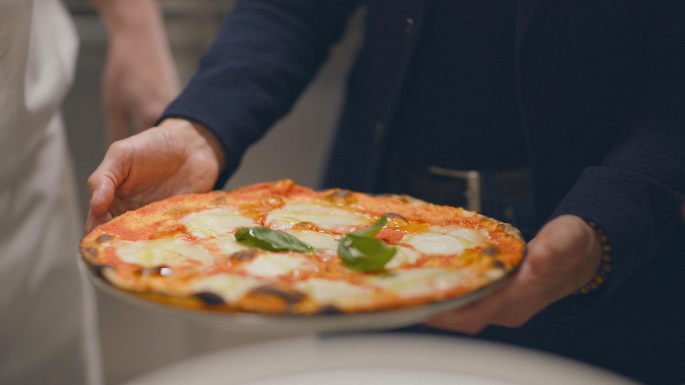 Ramadan El Sabawy hands Stanley Tucci a plate with his son's crispy, mouthwatering Margherita Pizza. [Photo of the day - May 2026]